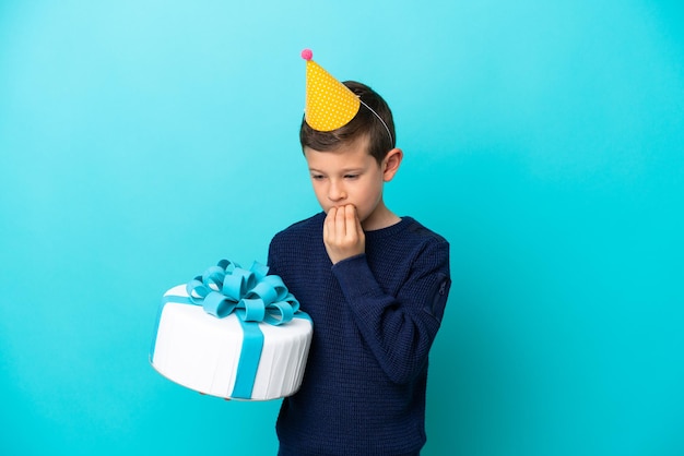 Little boy holding birthday cake isolated on blue background having doubts