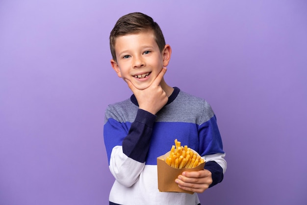 Little boy holding fried chips isolated on purple background happy and smiling