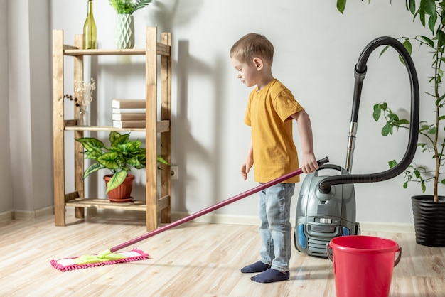 A little boy is cleaning the floor of a room using a mop. Concept of independence, help to parents, housework of the child