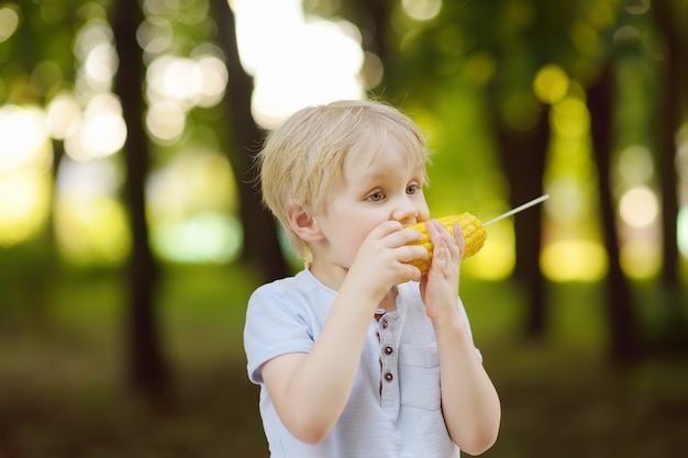 Little boy is eating corn outdoors. Street food for childs.