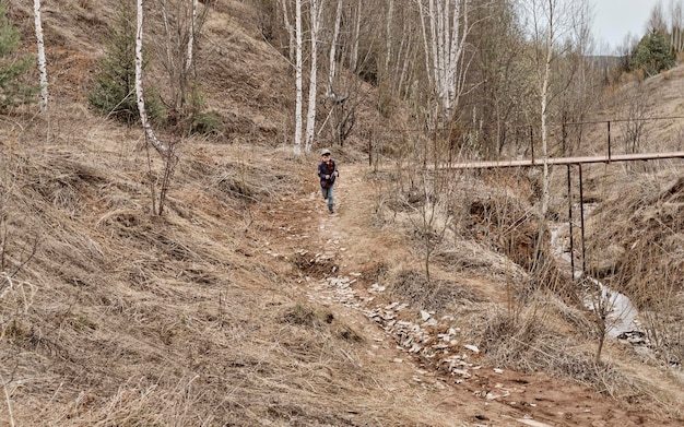 A little boy is running down from the hill on a cloudy autumn day A hill with dry grass sandy path childhood in countryside Lonely boy playing