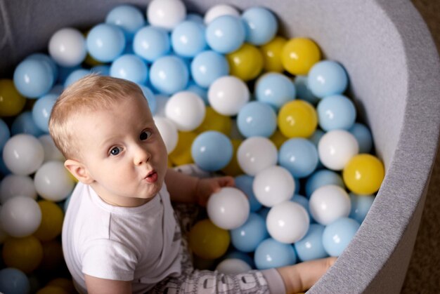 a little boy is sitting and playing in plastic balls. the child smiles