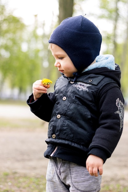 A little boy istands turning sideways and sniffing a flower crooks his face