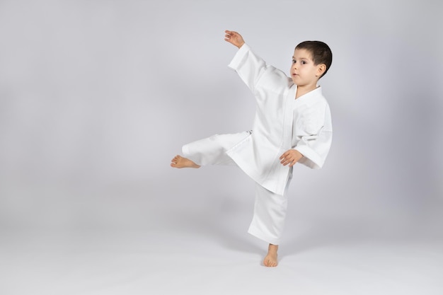 A little boy in a kimono practices karate on a white background