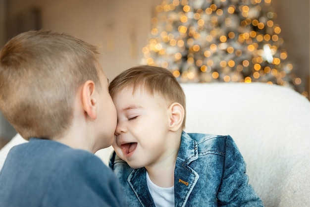 Little boy kissing his baby brother on Christmas morning. Kid boy tenderly kissing the forehead of his younger brother. The concept of love and friendship between siblings. New year's eve.