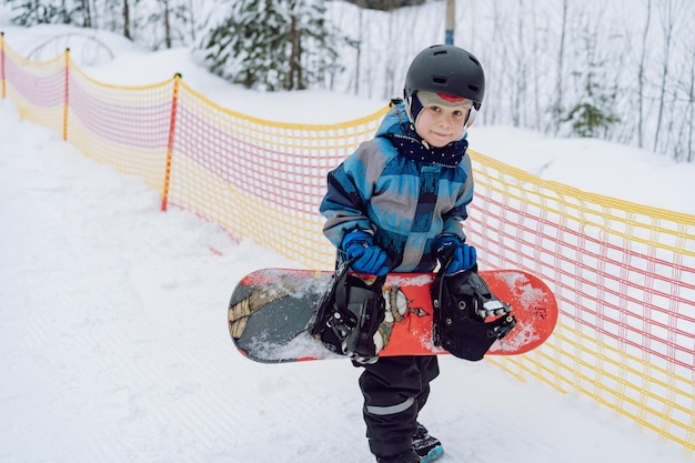 Little boy learning to ride on snowboard standing on ski slope Winter leisure