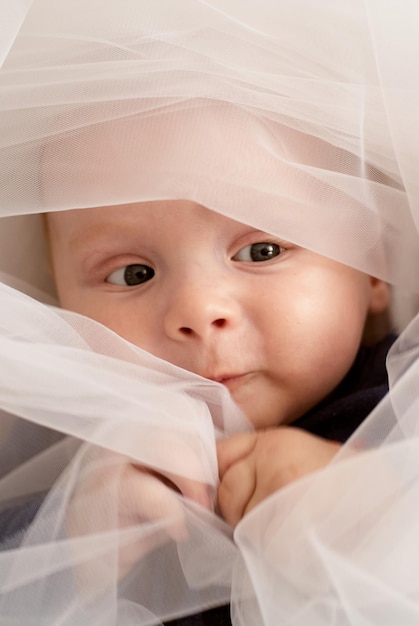 a little boy looks through the fabric. white fabric. portrait of the baby. the blue - eyed child