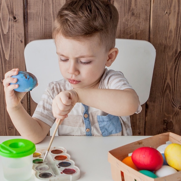 Little boy painting colorful eggs for easter on wooden background