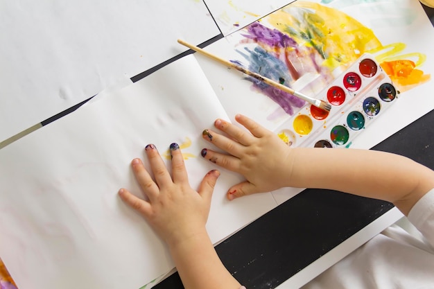 A little boy paints with watercolor paints on a table