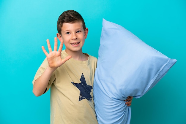 Little boy in pajamas isolated on blue background counting five with fingers