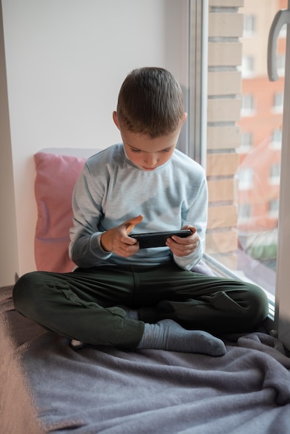 Little boy playing mobile game on smartphone sitting on a sofa top view Child leisure at home video