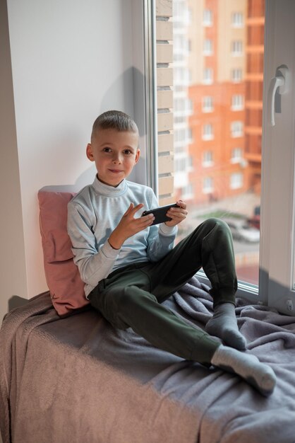 Little boy playing mobile game on smartphone sitting on a sofa top view Child leisure at home video