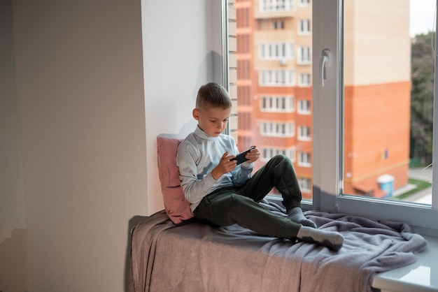 Little boy playing mobile game on smartphone sitting on a sofa top view Child leisure at home video