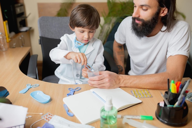 Little boy playing pretends like doctor examining a man in comfortabe medical office