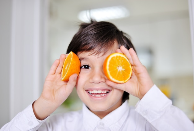 Little boy playing with orange slices on eyes as glasses