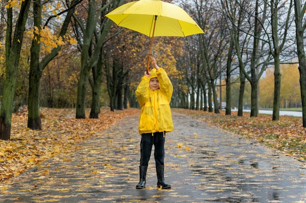 Little boy plays in park with a yellow umbrella Child walking on fall rainy street