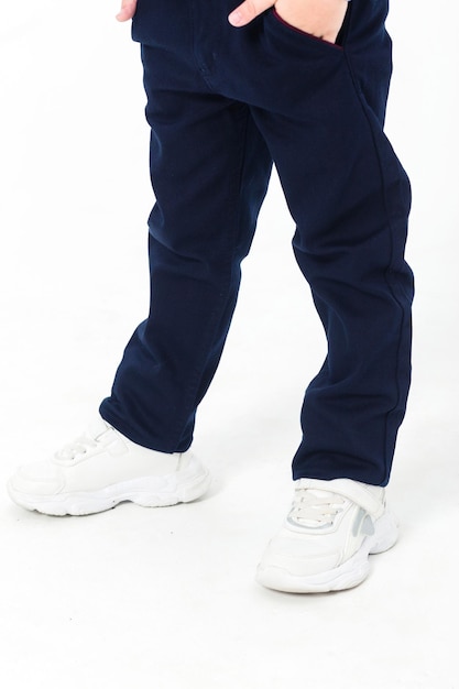 Little boy posing in school uniform in trousers and white sneakers on a white background Vertical photo