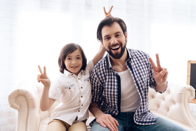 Little boy prankster puts horns to bearded man.