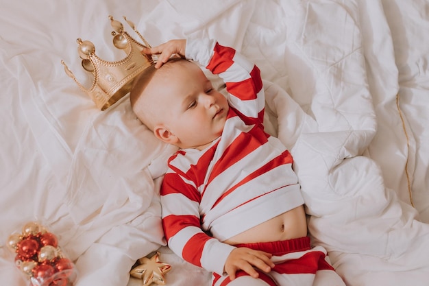 Little boy in red and white pajamas tries on a golden crown lying in bed