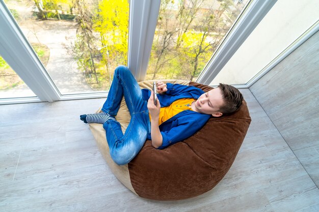 Little boy relaxing on a terrace and surfing the net on smart phone.