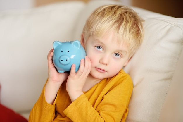 Little boy shaking a piggy moneybox and dreams of what he can buy.