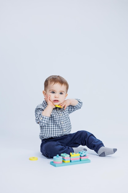 A little boy in a shirt is building a colorful wooden toy on a white background The concept of children's development games for children toys Copy space