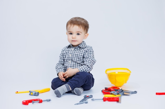 A little boy in a shirt with a helmet and a toy tool White background Toy construction tool for children