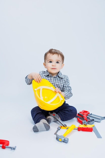 A little boy in a shirt with a helmet and a toy tool White background Toy construction tool for children