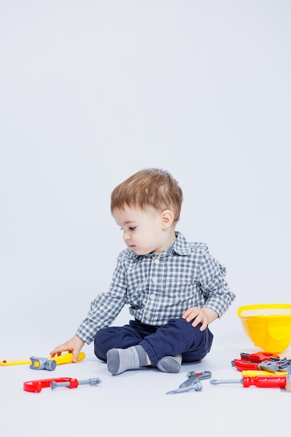 A little boy in a shirt with a helmet and a toy tool White background Toy construction tool for children