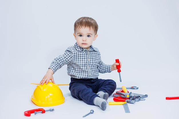 A little boy in a shirt with a helmet and a toy tool White background Toy construction tool for children