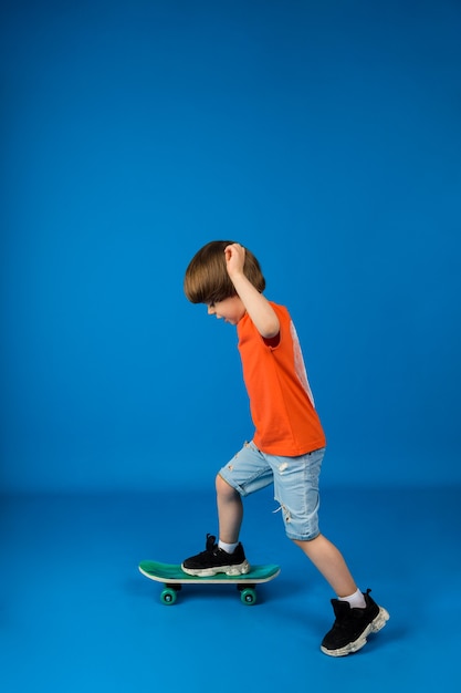 A little boy sideways rides a skateboard on a blue surface with space for text