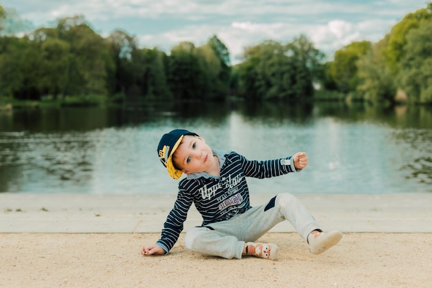 A little boy sits by the river on a sunny day