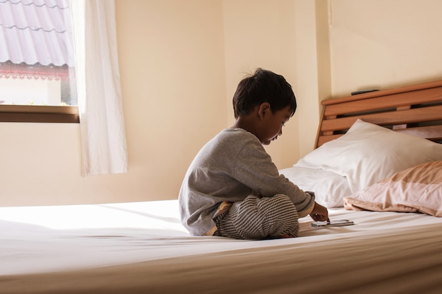 Little boy sitting on bed play smart phone in bedroom