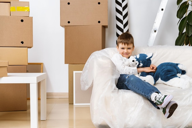 Little boy sitting on sofa with boxes on a moving day