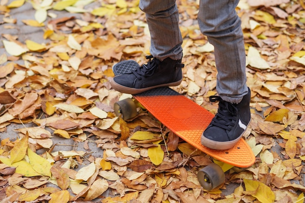 Little boy standing on a orange skateboard outdoors