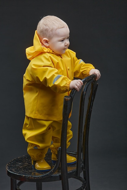 A little boy stands on chair in yellow firefighter suit