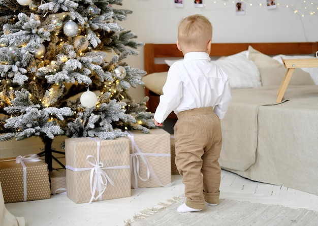 A little boy stands with his back to the camera and looks at the Christmas tree with a bunch of gifts