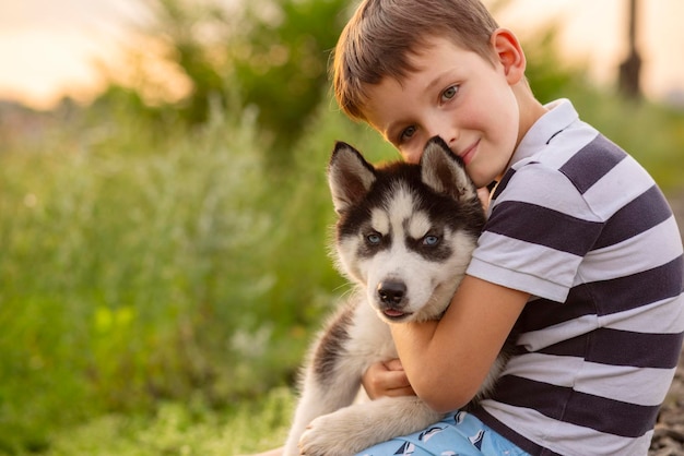 A little boy in a striped tshirt lovingly hugs his pet husky dog outdoors