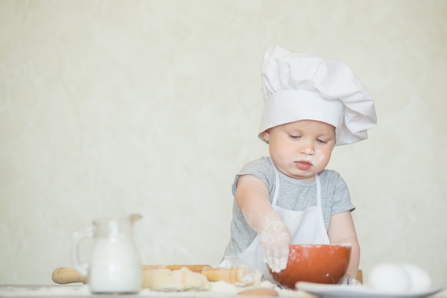 The little boy in a suit of the cook sculpts dough. Baby scullion make dinner in chef suit. Cooking concept