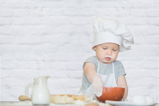 The little boy in a suit of the cook sculpts dough Baby scullion make dinner in chef suit