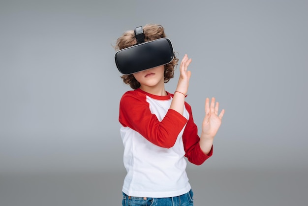 Little boy using virtual reality headset isolated on gray