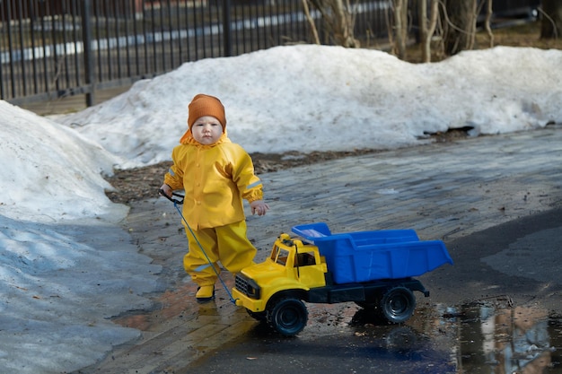 A little boy walks with a dump truck through puddles