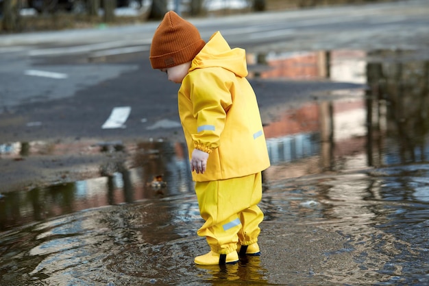 A little boy in a waterproof suit walks through puddles