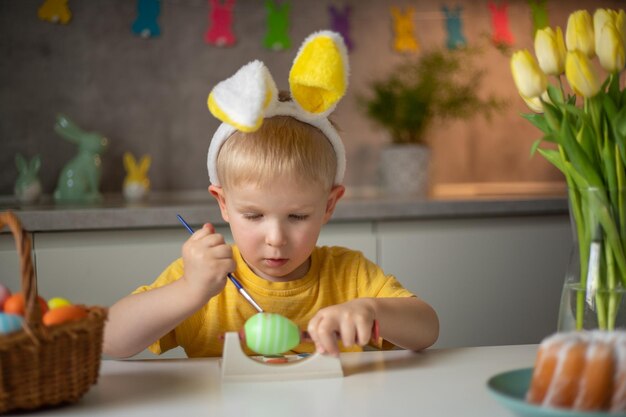 A little boy wearing bunny ears prepares painted Easter eggs for Easter while sitting at the kitchen table Happy easter