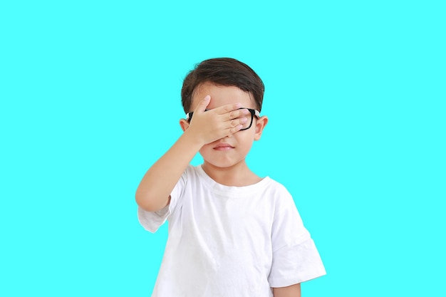 Little boy wearing glasses and closing hid eyes by one hand isolated on cyan background