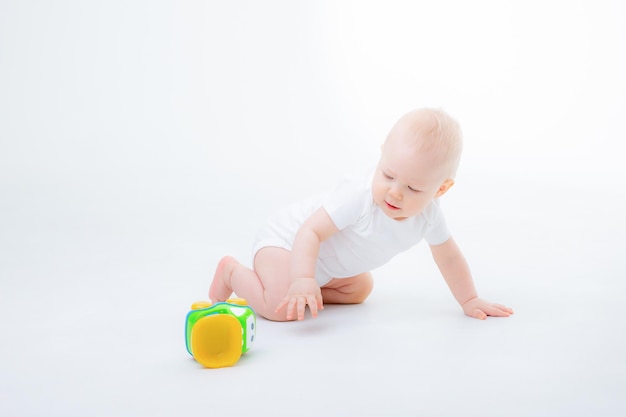 A little boy in a white bodysuit is sitting playing with a toy car, smiling on a white background