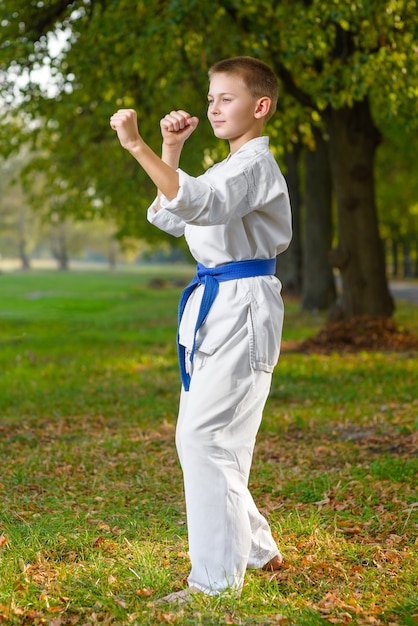 Little boy in white kimono during training karate exercises at summer outdoors