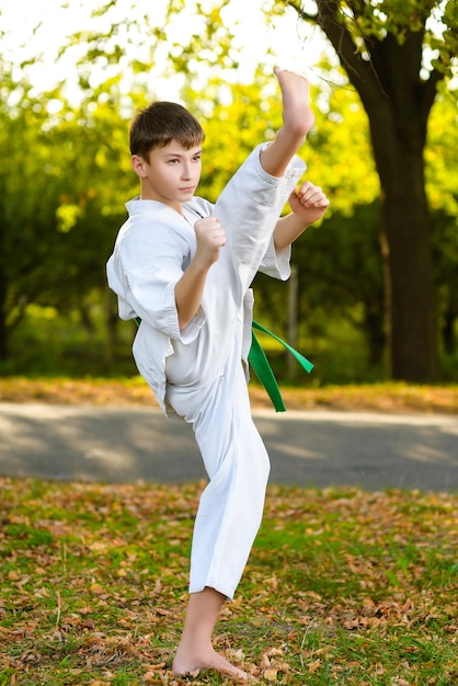 Little boy in white kimono during training karate exercises at summer outdoors