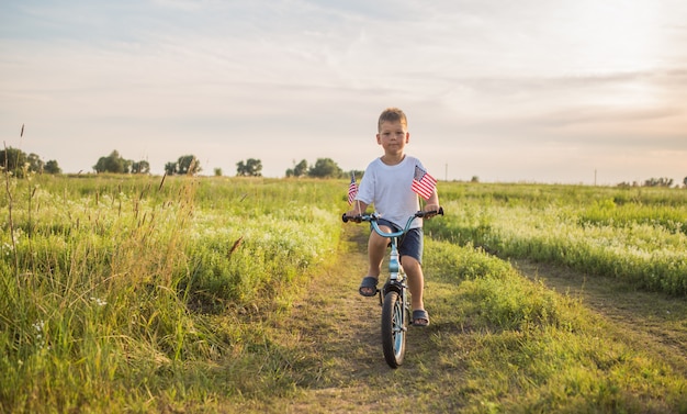 Little boy with American flag on his bicycle at the green field 