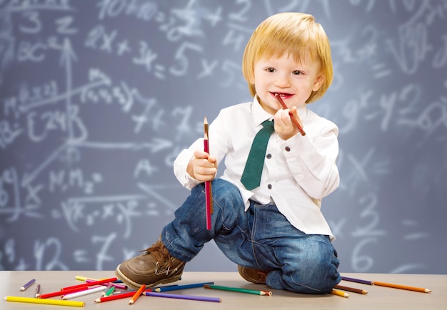 little boy with colored pencil with blackboard as background